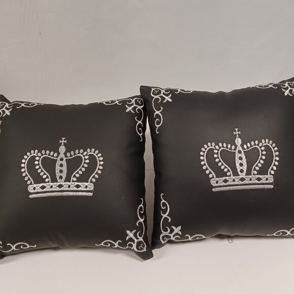 2 leather decorative pillows with crown embroidery.